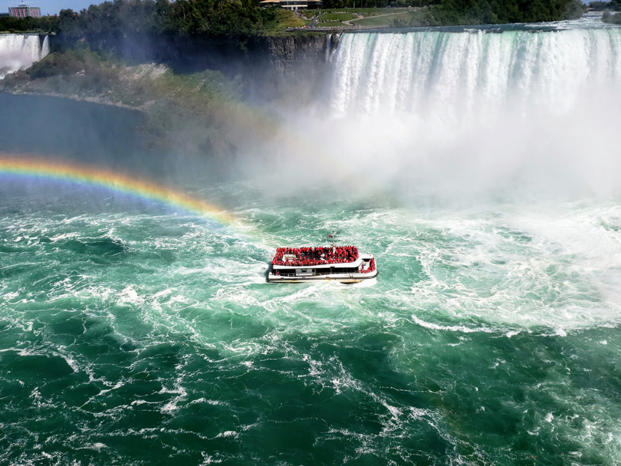 ferry boat in the middle of niagra falls with a rainbow on the left side