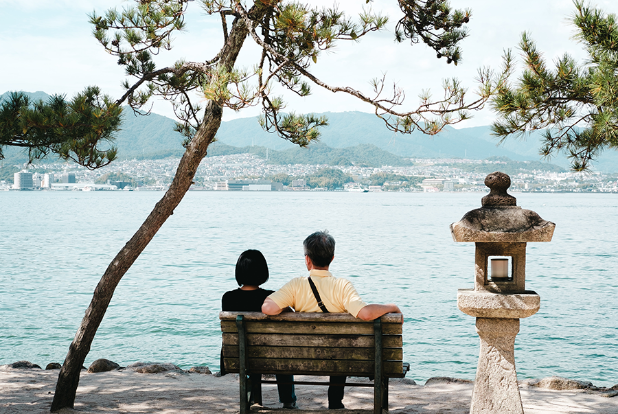 a couple sitting on a wooden bench by the water in Miyajima Island