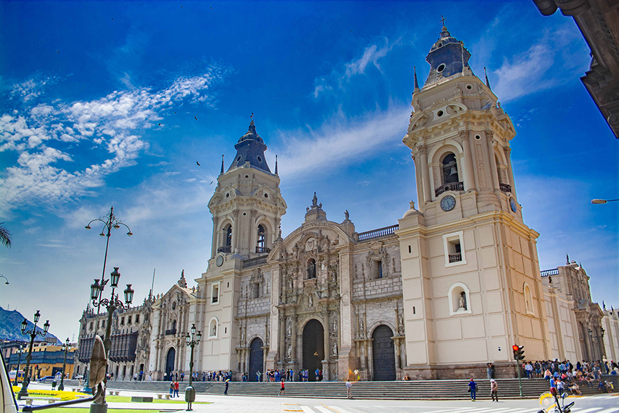 white cathedral in the center of lima, peru with blue skies brimming the plaza