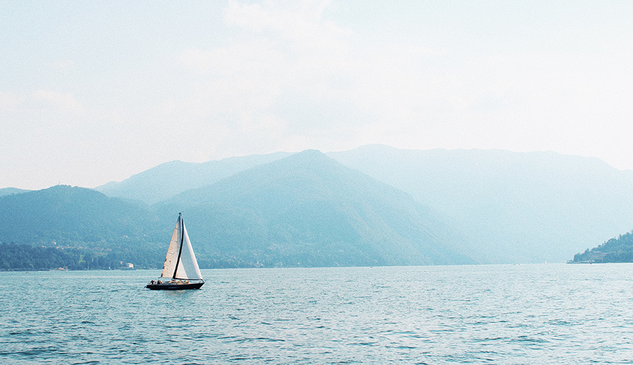 sailboat in the middle of lake como, blue skies, mountains in the background